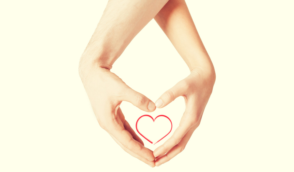 Two pairs of hands coming together to form a heart shape around a small, red-outlined heart icon on a white background.
